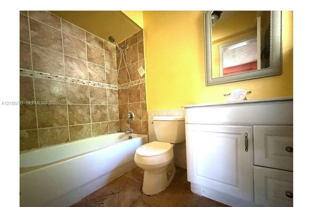 Bathroom featuring a white vanity cabinet with countertop basin, tub-and-shower combination with tiled surround, and a wall-mounted mirror