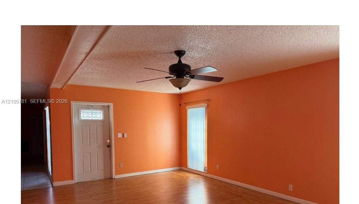 Room featuring wood-finish flooring, a ceiling fan with integrated lighting, and a six-panel exterior door with a decorative glass insert