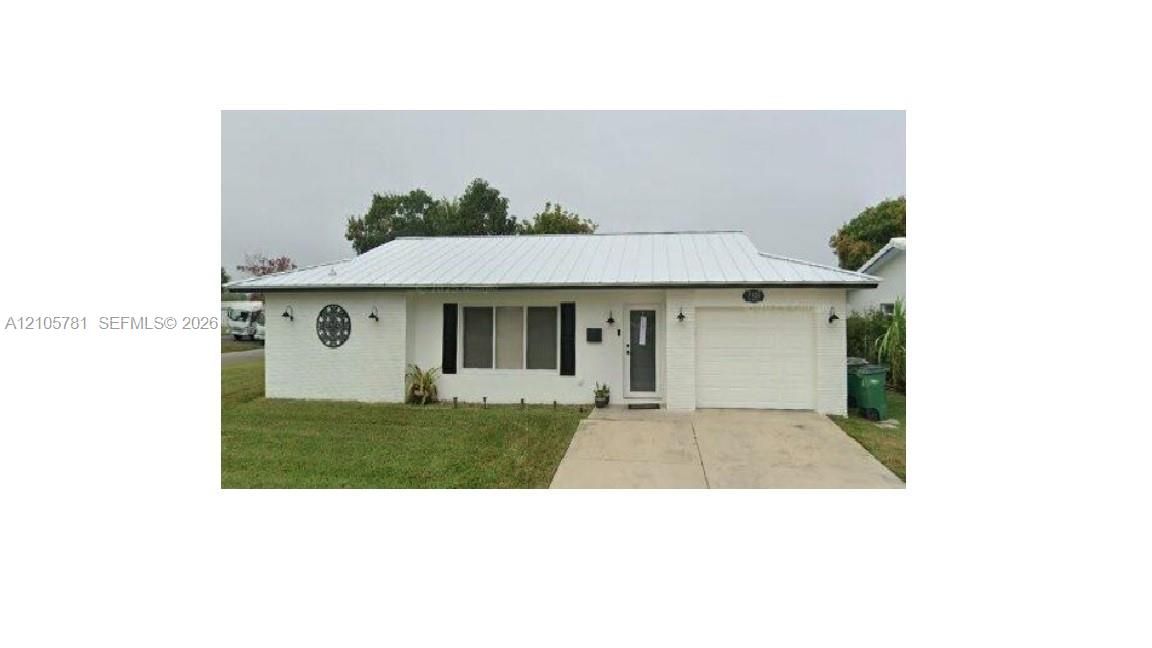 Single-story residence featuring white painted brick masonry, a standing seam metal roof, attached single-car garage, and concrete driveway