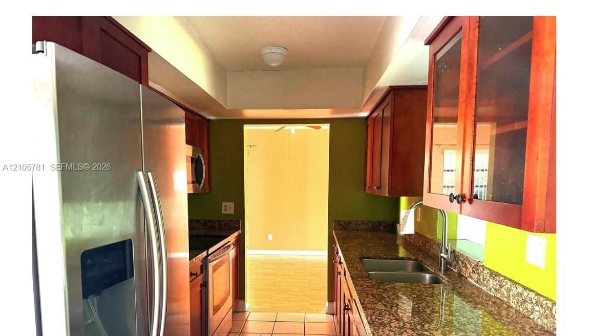 Kitchen featuring natural wood-finish cabinetry, stone-surface countertops, stainless steel appliances, a dual-basin undermount sink with a pull-down faucet, and upper glass-front display cabinets