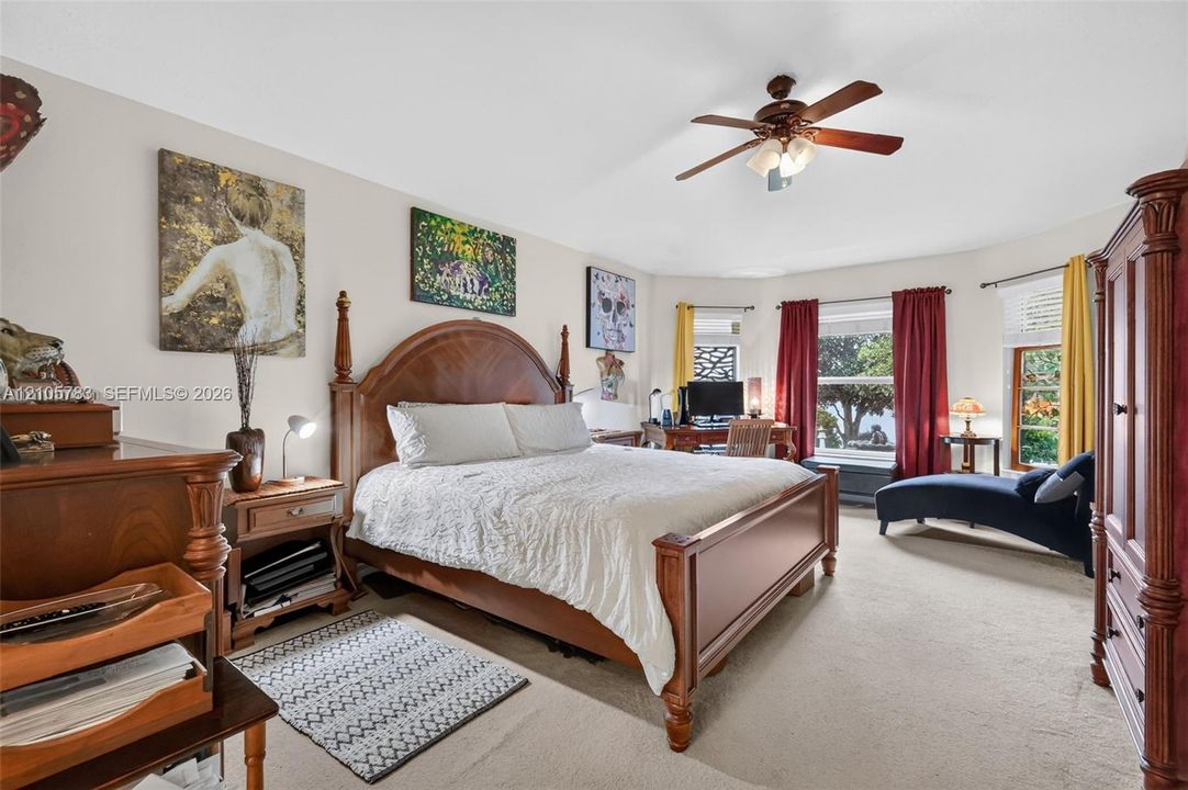 Spacious room featuring neutral carpeting, a multi-pane bay window, and a ceiling fan with integrated lighting
