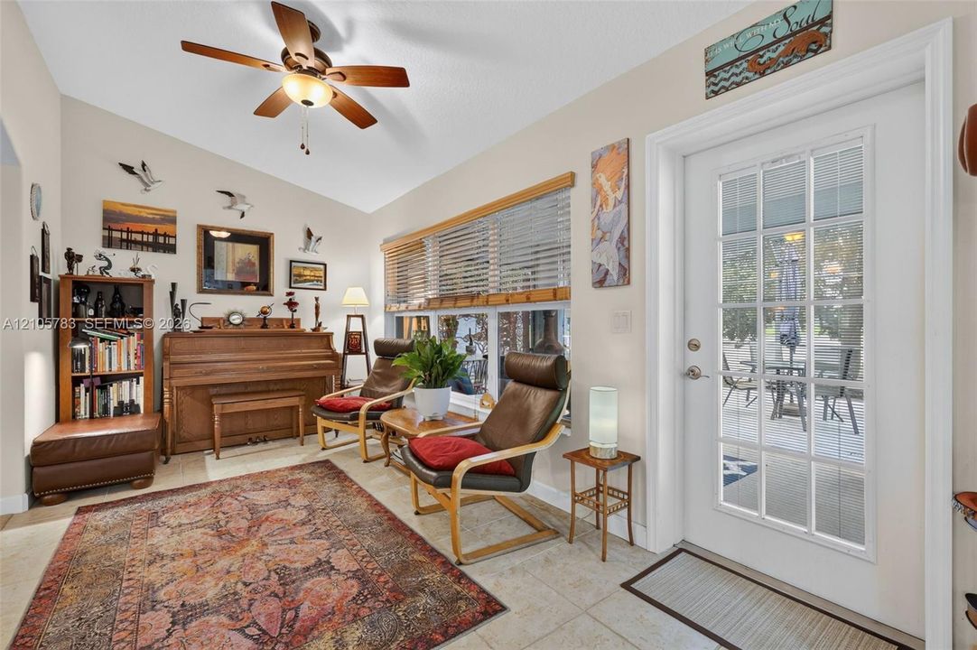 Vaulted ceiling with a wood-tone ceiling fan, light-colored tile flooring, oversized horizontal window with blinds, and a multi-pane glass-panel exterior door