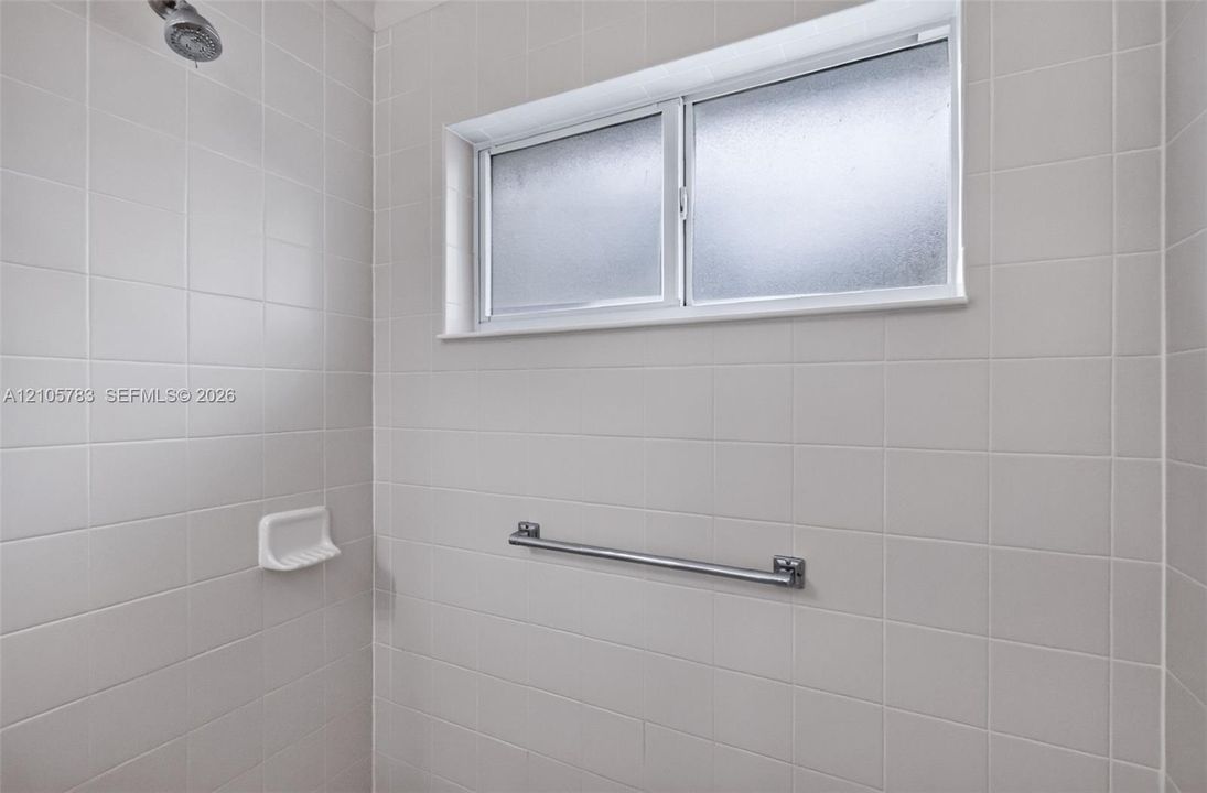 Tiled shower surround featuring a built-in recessed soap dish, a horizontal stainless steel grab bar, and an elevated sliding window with obscured glass