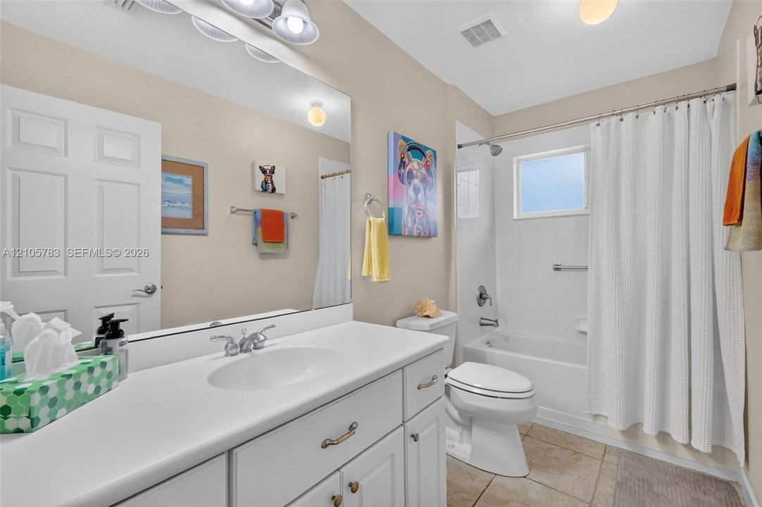 White vanity with integrated basin and countertop, expansive wall-mounted mirror, three-light fixture, and ceramic tile flooring