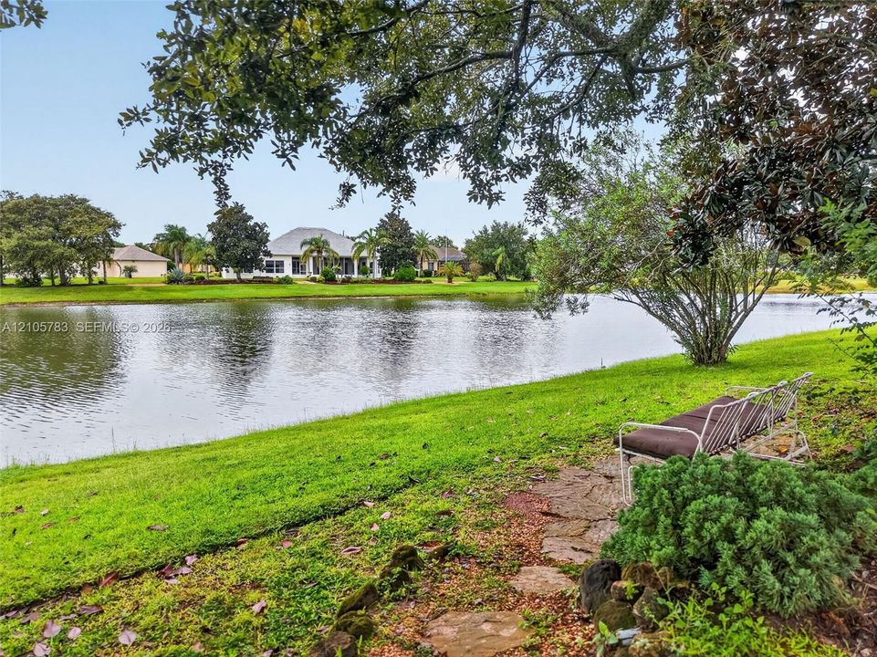 Waterfront parcel featuring a natural pond, stone-laid pathway, mature trees, and landscaped lawn
