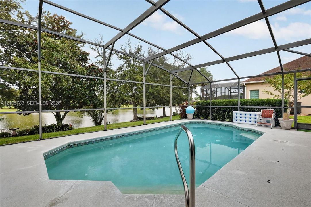 Screened-in pool deck featuring a concrete patio, metal pool enclosure, in-ground swimming pool, and metal handrail