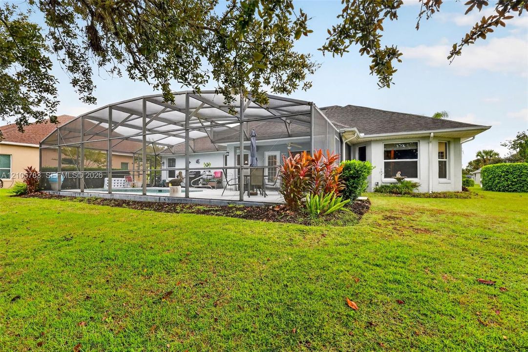 Screened-in pool enclosure featuring a concrete patio, landscaped garden beds, multi-faceted roofline, and siding exterior