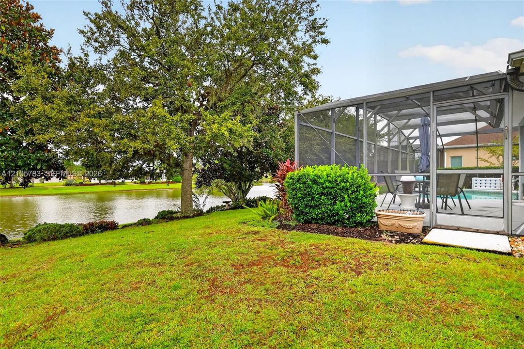 Screened lanai featuring a concrete patio, mature landscaping, expansive lawn, and direct water frontage