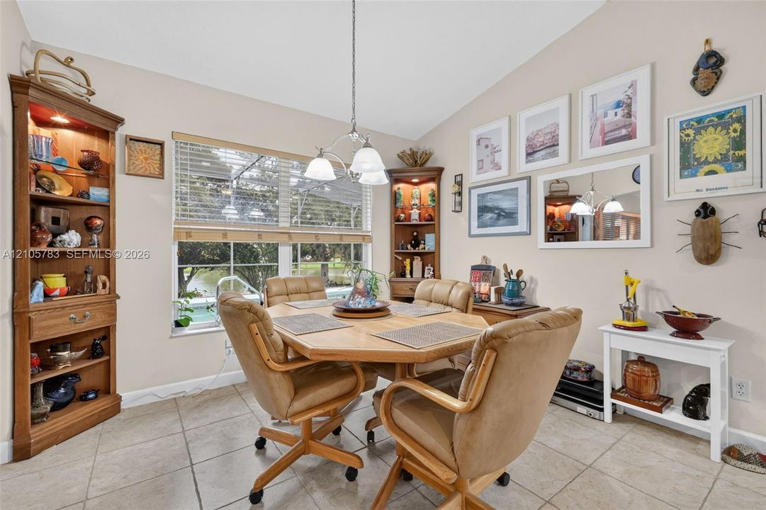 Dining area featuring vaulted ceilings, light-colored tile flooring, custom built-in cabinetry with integrated lighting, and a multi-light chandelier