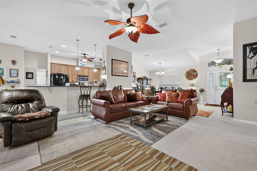 Open-concept interior featuring vaulted ceilings, recessed lighting, a kitchen breakfast bar, and decorative ceiling fan fixtures