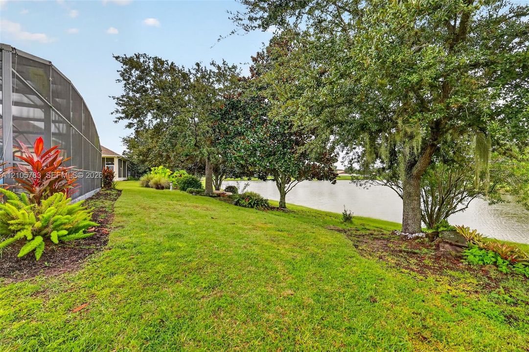 Exterior area featuring a screened-in enclosure, manicured lawn, mature trees, and waterfront perimeter