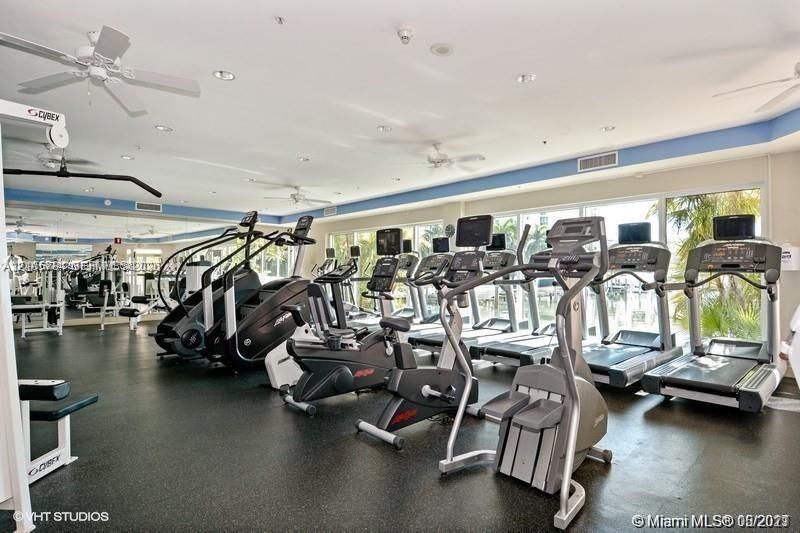 Fitness center featuring floor-to-ceiling windows, mirrored walls, ceiling-mounted fans, and rubberized flooring