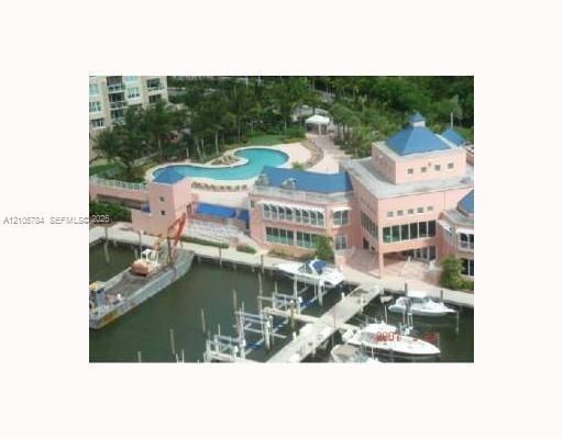 Waterfront property featuring a private boat slip, a multi-level clubhouse with blue metal roofing, and an outdoor swimming pool surrounded by paved decking and landscape greenery