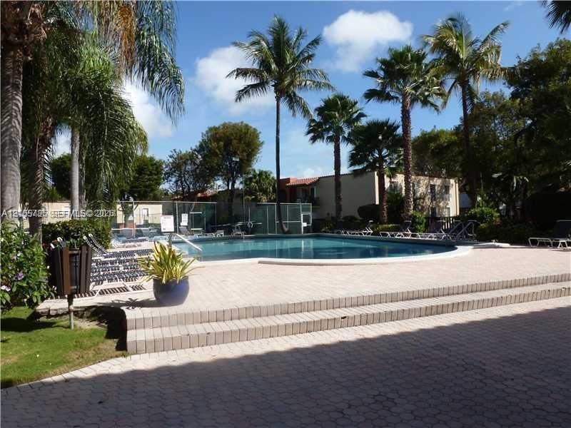 In-ground swimming pool featuring concrete paver decking, multi-level stairs, perimeter fencing, and surrounding palm trees