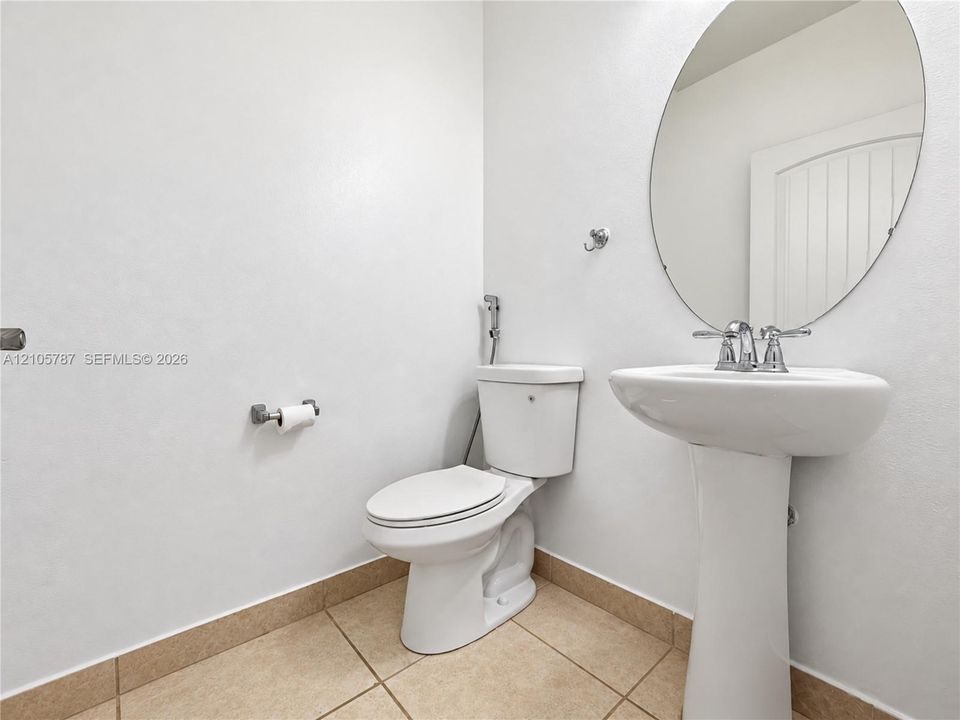 Bathroom featuring a white pedestal sink, polished chrome faucet, oval wall-mounted mirror, and tile flooring