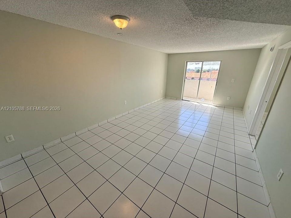 Spacious room featuring white tile flooring, neutral wall tones, a ceiling-mounted light fixture, and glass sliding doors