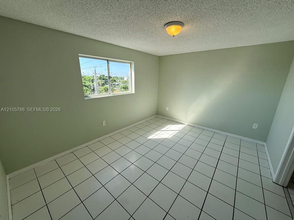 Neutral-toned interior space featuring light-colored square floor tiles, a single sliding window, and a central ceiling-mounted light fixture