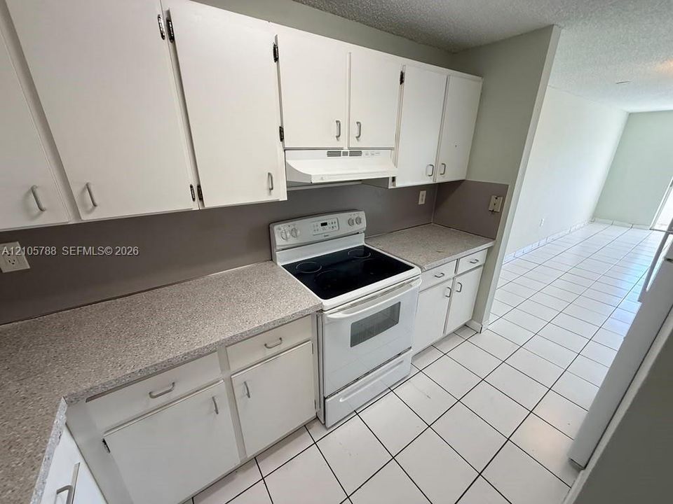 Kitchen featuring white cabinetry, solid-surface countertops, electric range, range hood, and ceramic tile flooring