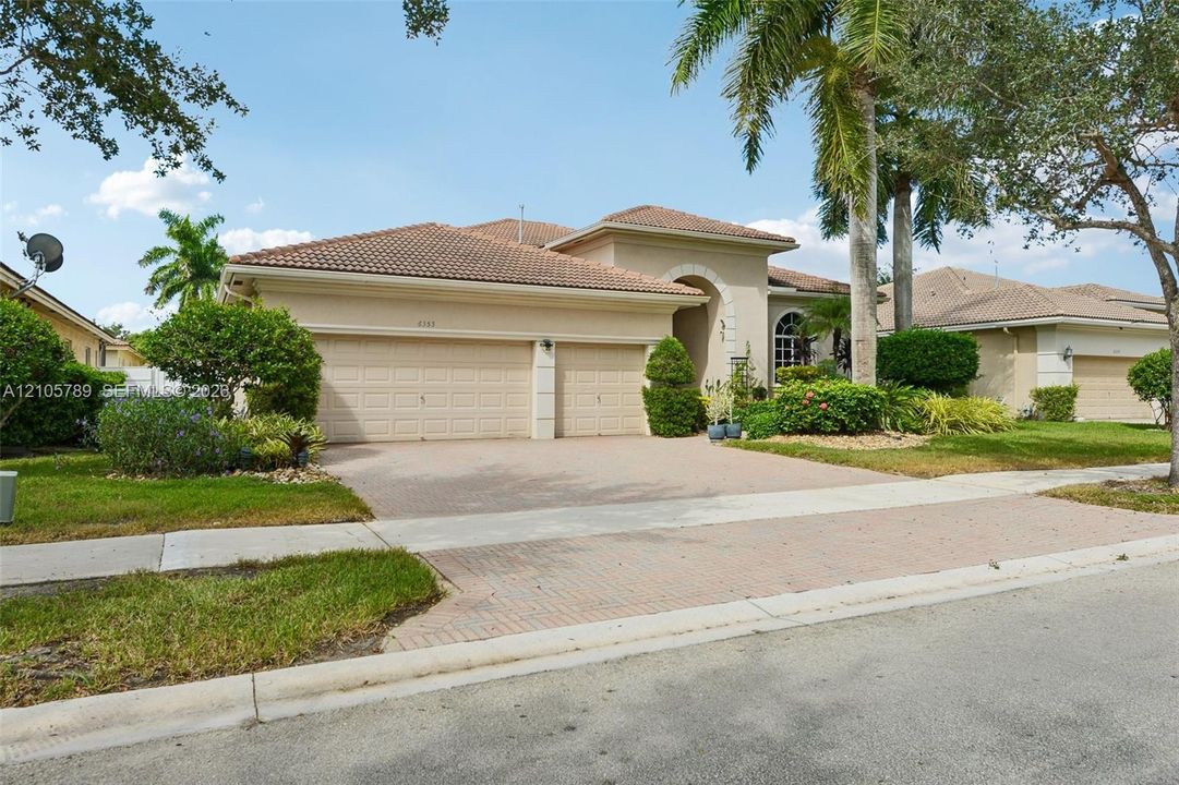 Stucco exterior featuring a tile roof, arched entryway, and multi-car garage with paver driveway