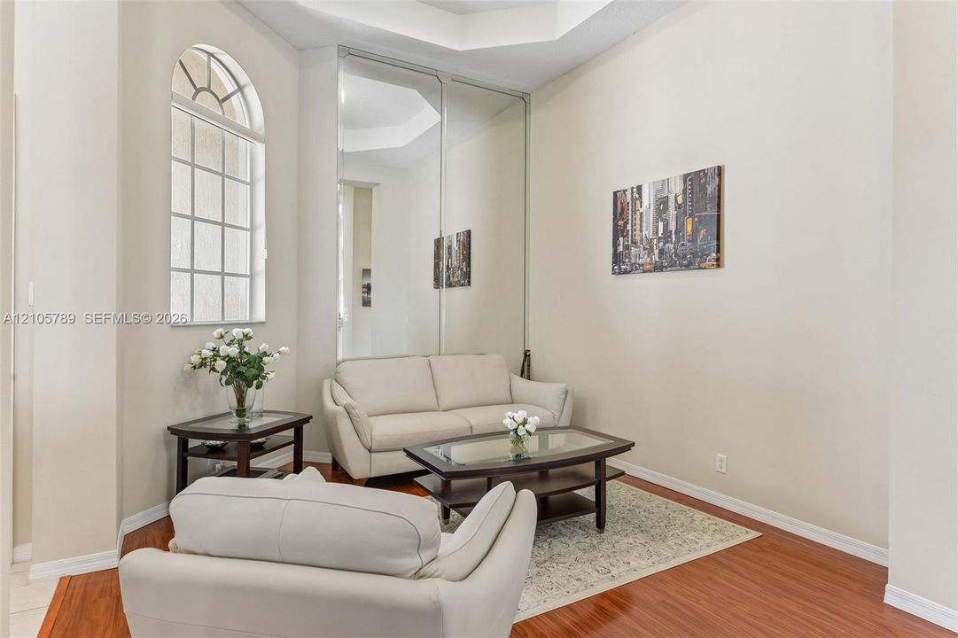 Room featuring high ceilings, wood-finish flooring, an arched window, and floor-to-ceiling mirrored panels