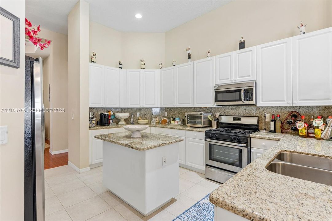 Kitchen featuring white shaker-style cabinetry, stone-finish countertops, central island, dual-basin stainless steel sink, and stainless steel appliances