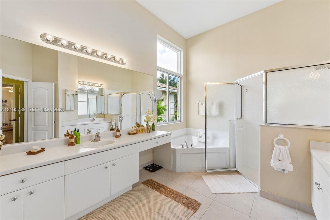 Bathroom featuring a dual-sink vanity with white cabinetry and solid-surface countertops, a corner soaking tub, and a glass-enclosed shower