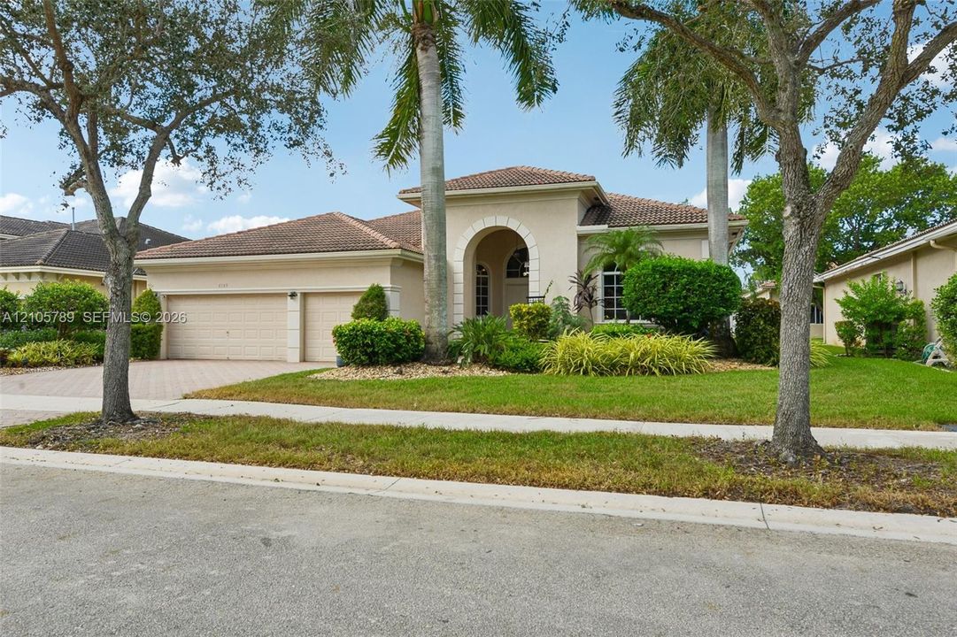 Stucco exterior featuring an arched entryway, a tile roof, a three-car garage, and a brick-paver driveway