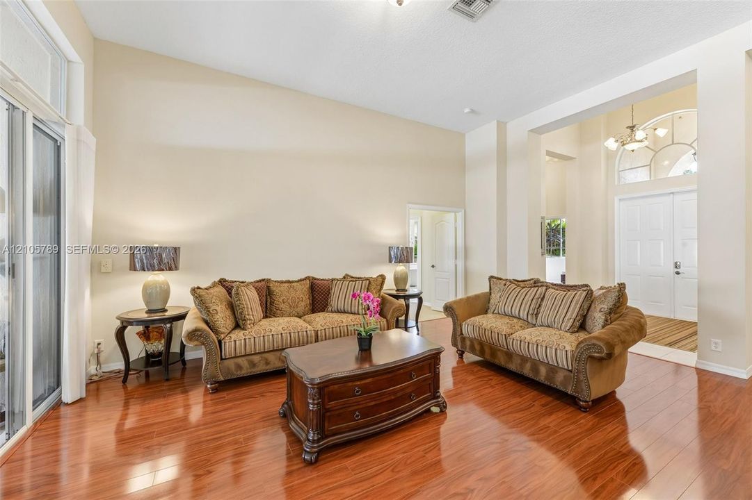 High-ceiling interior featuring wood-finish flooring, recessed lighting, double-door entry with an arched transom window, and sliding glass doors