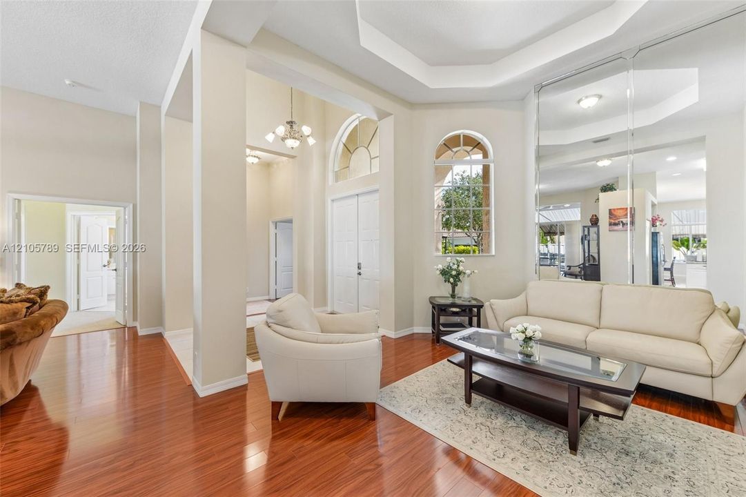 Living area featuring high ceilings with crown molding, wood-finish flooring, full-wall mirrors, arched windows, and double-entry doors
