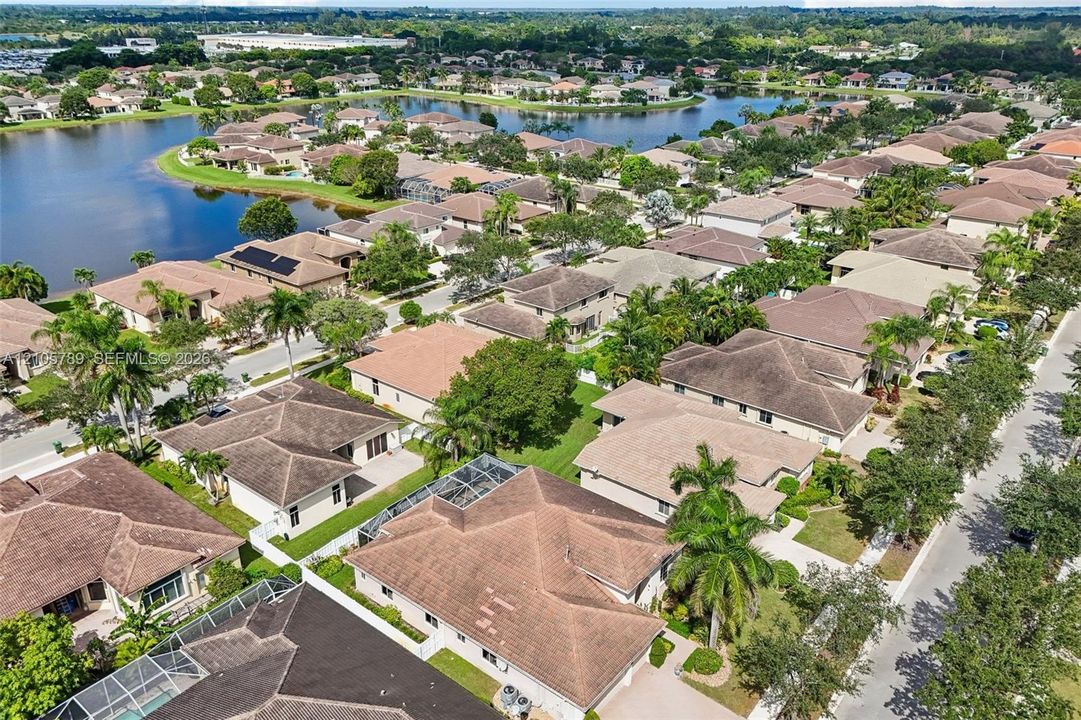 Aerial perspective featuring a residential community with tiled-roof structures, screen-enclosed pool enclosures, established landscaping, and a central lake