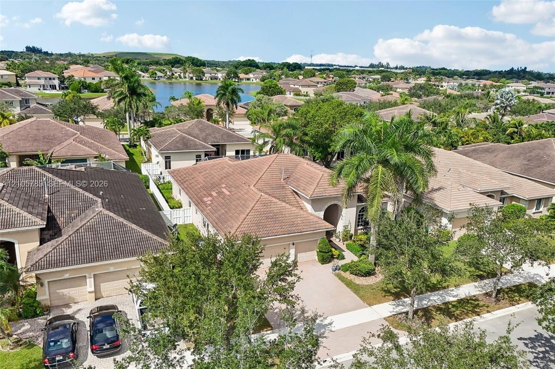 Aerial perspective of a single-story residence featuring a multi-pitched tile roof, concrete paver driveway, two-car garage, and mature palm landscaping