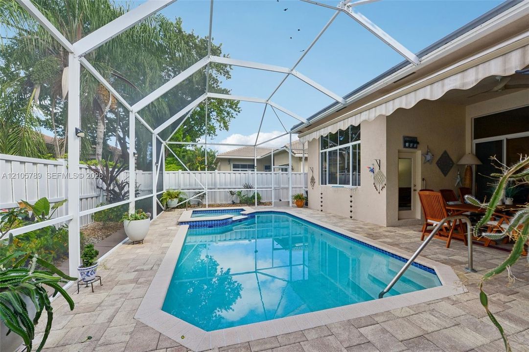 Screened-in patio featuring a swimming pool with an integrated spa, stone-paver decking, and white vinyl privacy fencing