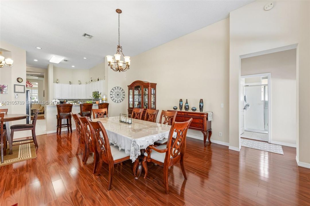 Open-concept floor plan featuring high ceilings, wood-finish flooring, a multi-tiered breakfast bar, and a decorative chandelier