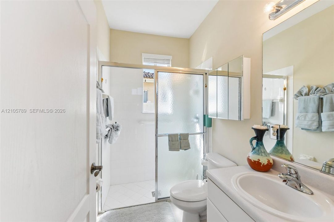 Bathroom featuring a glass-enclosed shower, white vanity with an integrated sink, polished chrome faucet, and tri-fold mirrored medicine cabinet