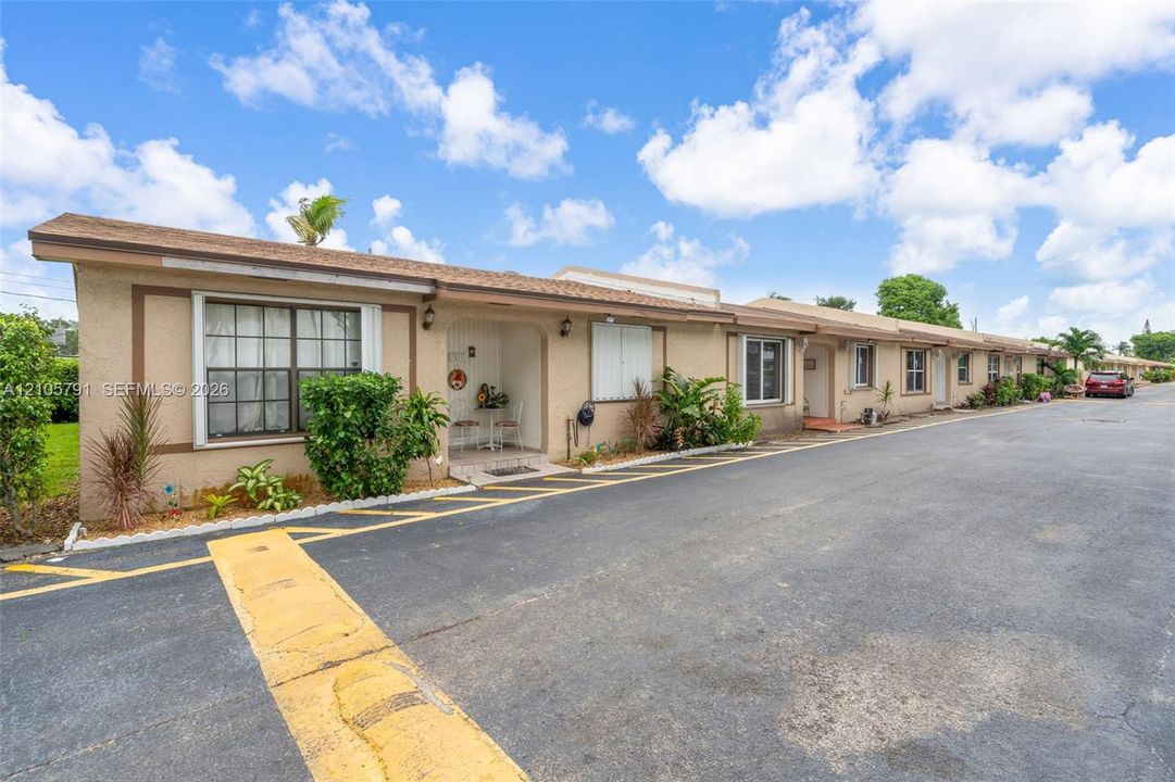 Single-story exterior featuring a stucco facade, neutral-toned finish, grid-pattern windows, recessed entryways, and asphalt parking area