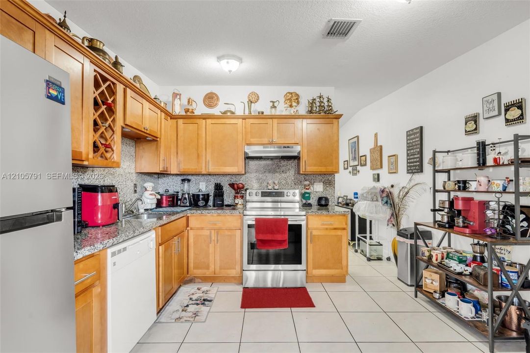 Kitchen featuring natural-finish wood cabinetry, integrated wine storage, stone-patterned countertops, tile flooring, and stainless steel appliances