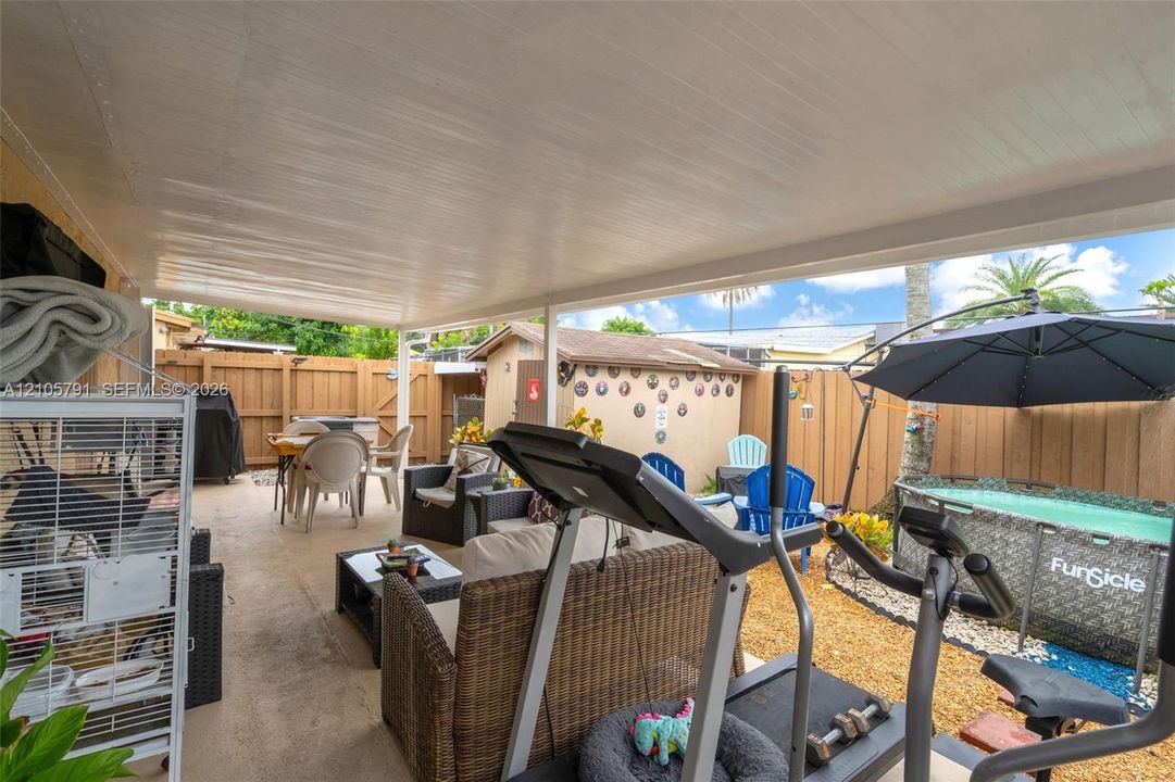 Covered concrete patio featuring a wooden perimeter privacy fence, exterior storage shed, and gravel landscaping