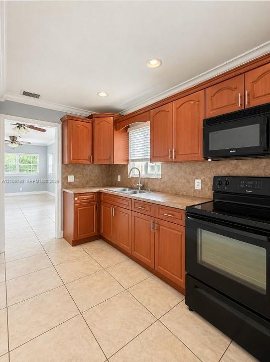 Kitchen featuring wooden cabinetry, solid surface countertops, a tiled backsplash, black built-in appliances, and tile flooring