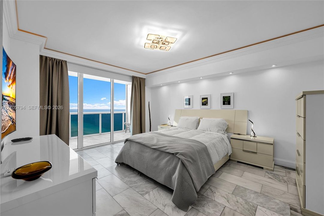 Stone flooring, recessed ceiling lighting, decorative crown molding, and floor-to-ceiling glass doors opening to a balcony with ocean exposure