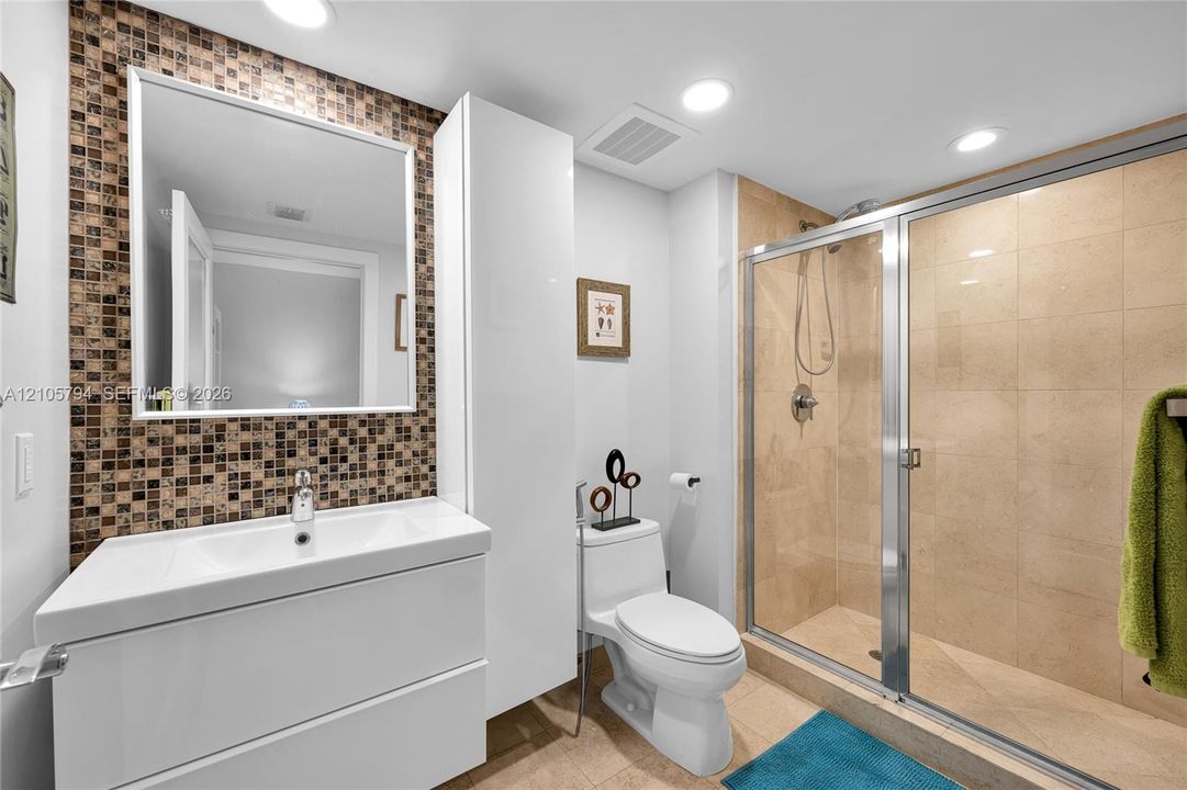 Bathroom featuring a white floating vanity, glass-enclosed shower with tiled walls, mosaic tile backsplash, and built-in vertical cabinetry