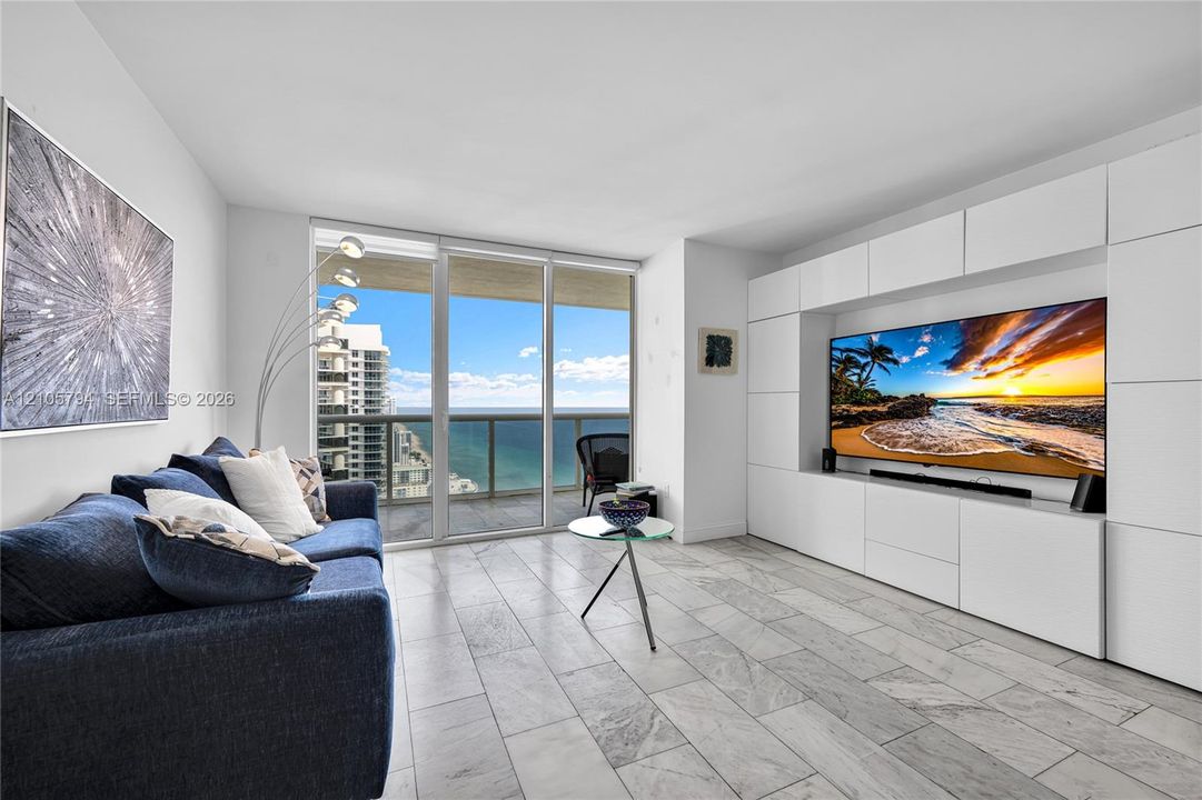 Living area featuring large-format tile flooring, floor-to-ceiling glass doors, and a custom built-in white cabinetry wall unit