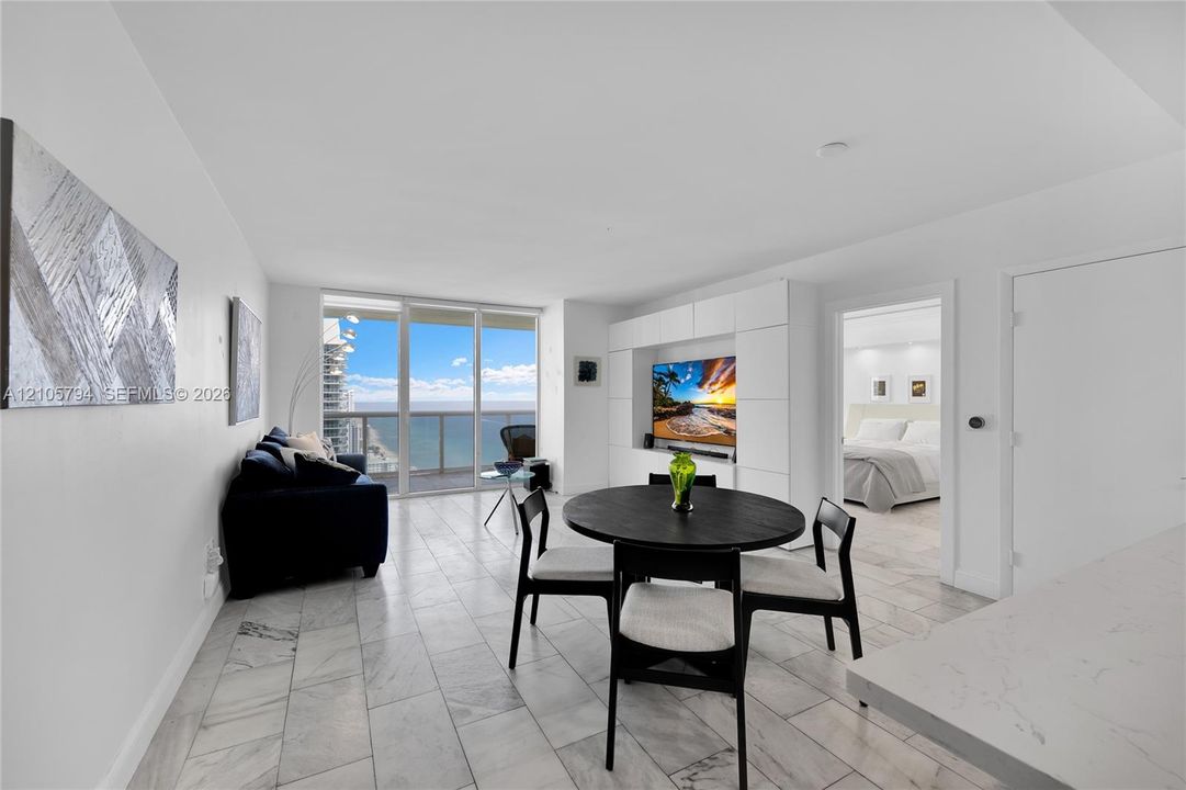Floor-to-ceiling glass sliding doors, stone-finish tile flooring, built-in white wall cabinetry, and ocean backdrop