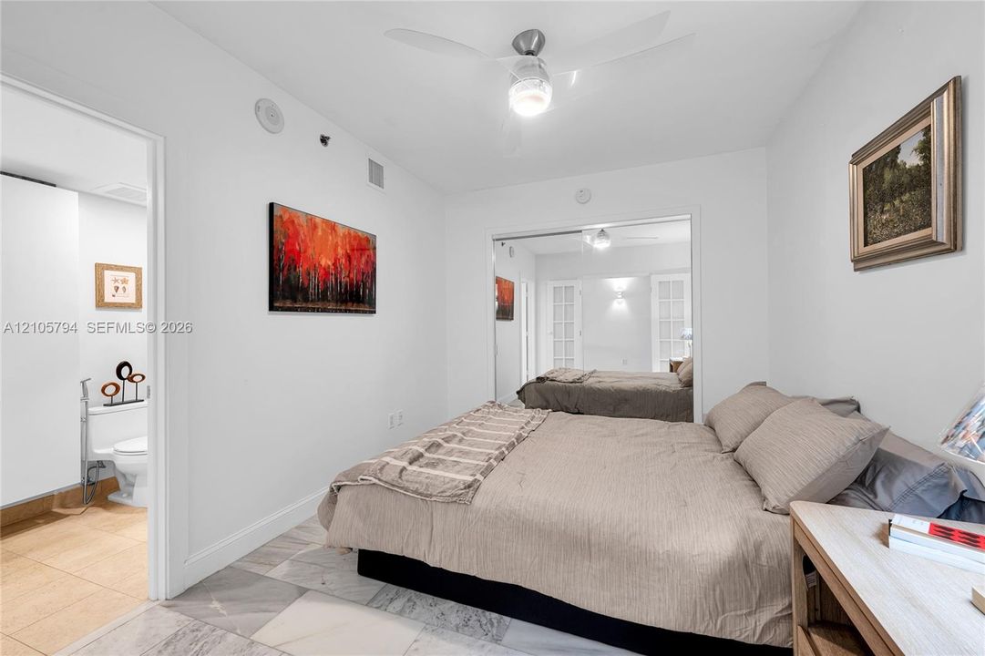 Light-toned stone tile flooring, mirrored closet doors, and a ceiling-mounted light fixture with an integrated fan