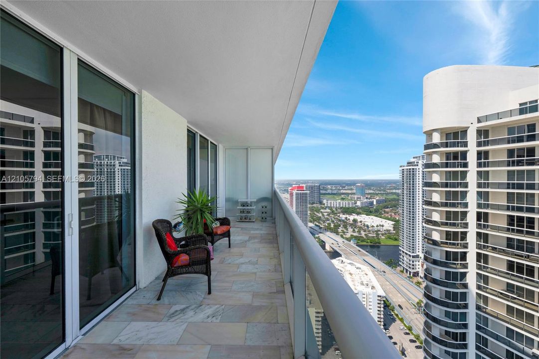 Covered balcony featuring natural stone flooring, full-height sliding glass doors, and a metal railing