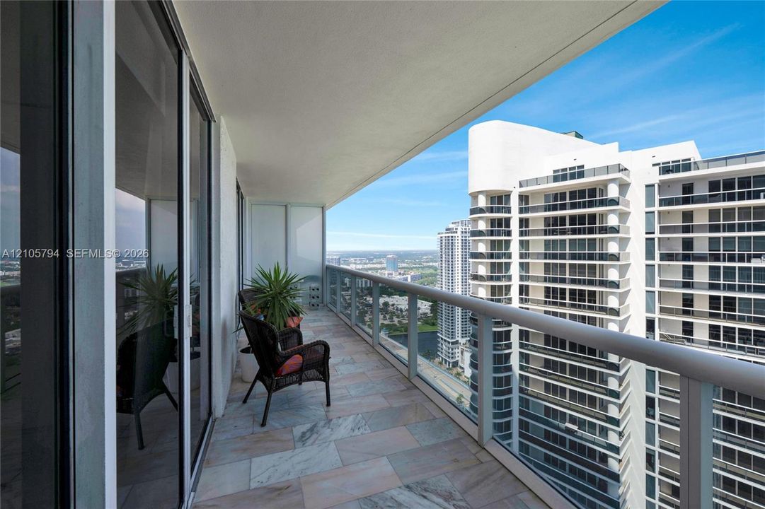 Covered balcony featuring stone tile flooring and a glass panel railing