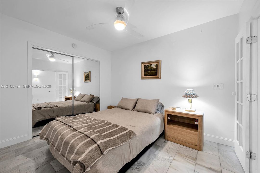 Room featuring stone-finish flooring, sliding mirrored closet doors, a ceiling fan with integrated lighting, and a French-style door