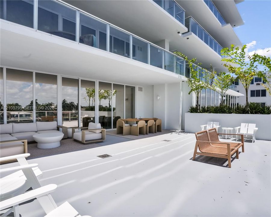 Expansive covered terrace featuring floor-to-ceiling glass doors, sleek glass balcony railings, a concrete floor surface, and integrated built-in planters