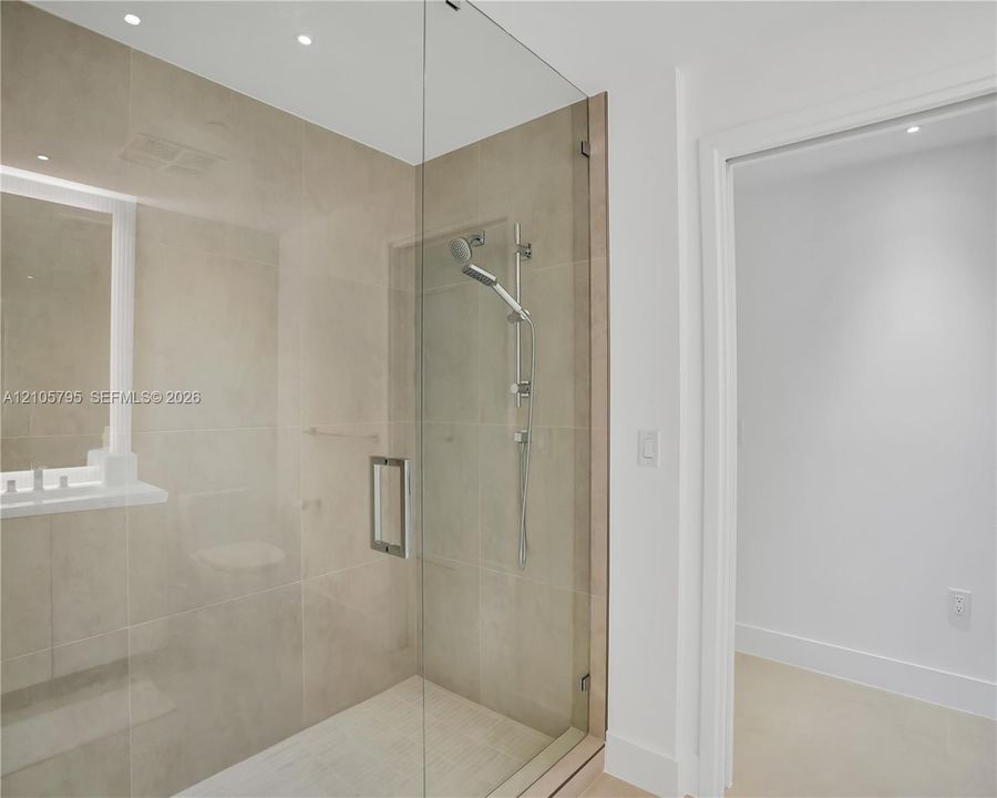 Walk-in shower featuring large-format neutral wall tile, a glass enclosure, an adjustable-height handheld showerhead, and recessed lighting