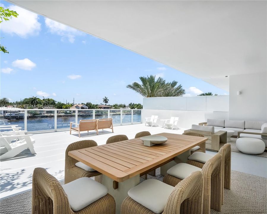 Expansive covered terrace featuring light-toned flooring, glass panel railings, and direct water frontage