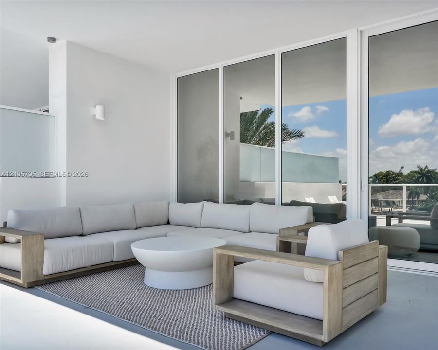 Covered patio featuring white-frame floor-to-ceiling glass sliding doors, smooth concrete flooring, and minimalist wall-mounted light fixtures